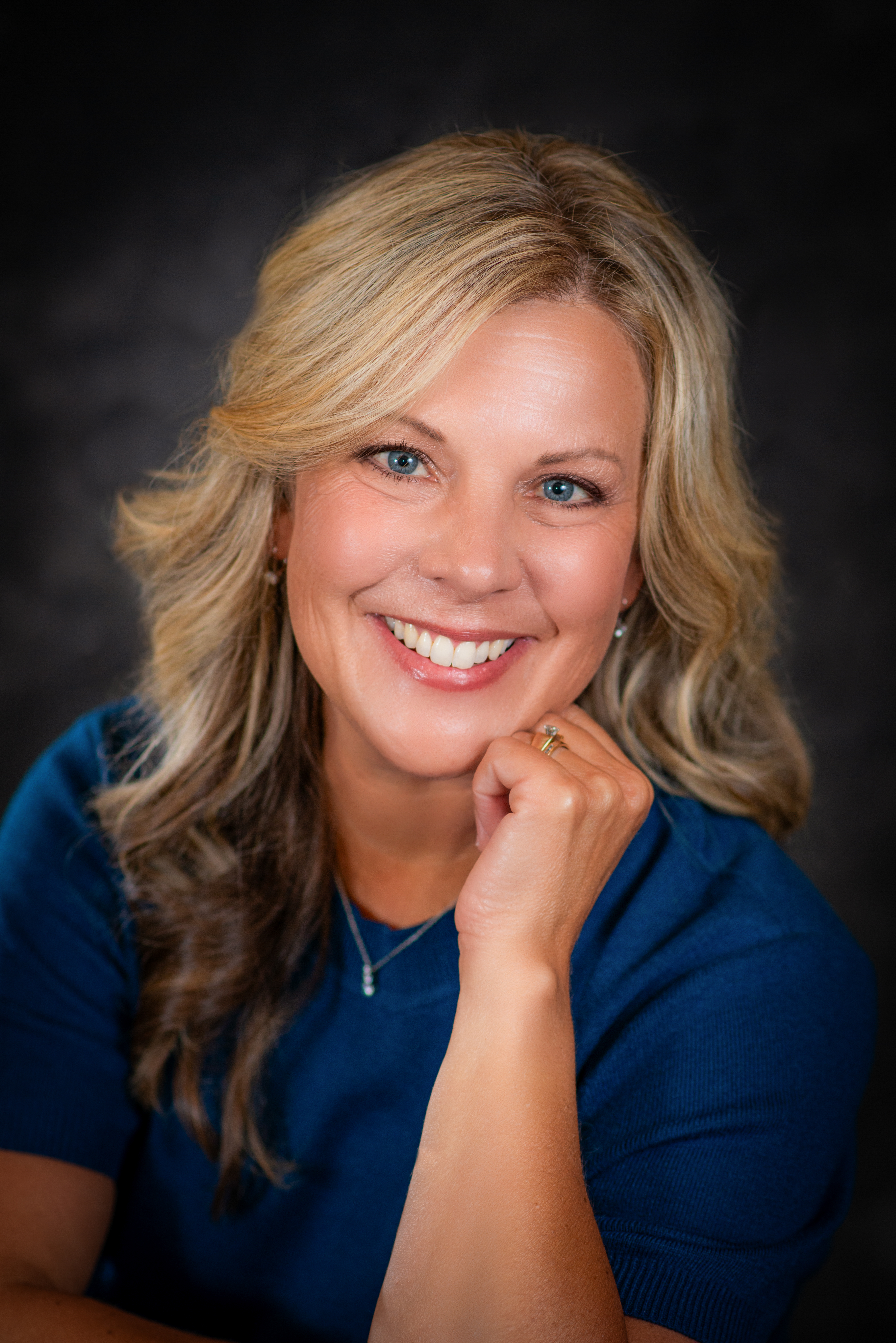 Professional photo of Tracy Zamarron wearing a blue shirt smiling at the camera with hand near face.
