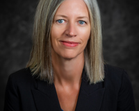 Headshot of Theresa Rowland wearing a blakc blazer with a blue shirt underneath. She has gray/blonde hair and blue eyes.