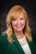 Dr. Jodi Bennett wearing a white lace shirt and kelly green blazer. She has blonde hair and blue eyes. 
