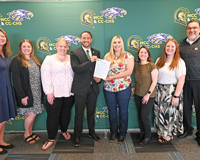 MCC staff and Carson City-Crystal schools staff pose in front of a backdrop featuring both schools logos with a paper copy of the new direct admissions agreement.