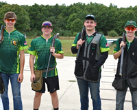 Four members of the MCC clay target shooting team pose for a photo with their shotguns draped over their shoulders.