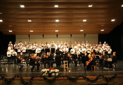 A large orchestra, choir and the conductor are photographed performing on a stage.